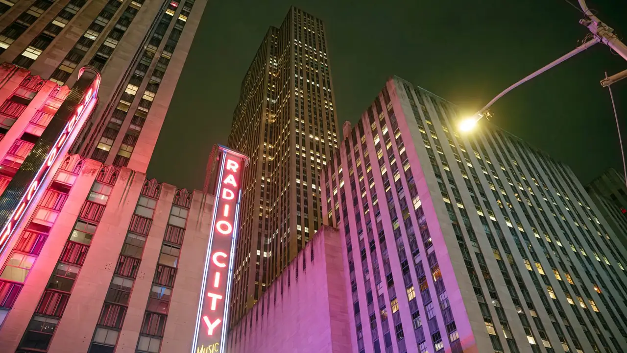 La torre verticale del Radio City Music Hall illuminata di notte fra i grattacieli del Rockefeller Center